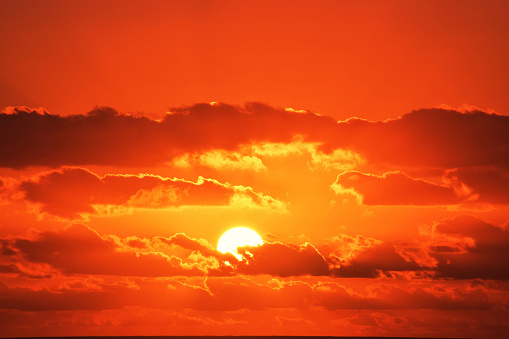 A golden Sun turns the early morning sky red as it breaks through clouds on Queensland's Gold Coast. The Pacific Ocean and horizon can be seen at the very bottom of frame.  Die to the composition and colour of the sky, this image could be used to address an range of topics and themes including holidays, seasons, time of day, climate change or environment.