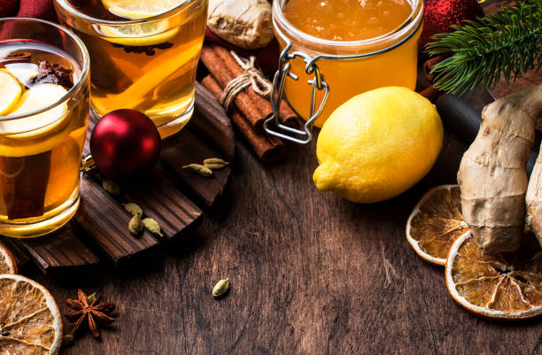 té caliente de invierno con fruta, limón y especias en copa de cristal con vapor en navidad o set de mesa de año nuevo, fondo rústico de madera - ginger tea cup cold and flu tea fotografías e imágenes de stock