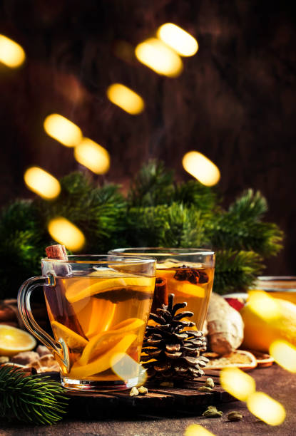 té caliente de invierno con fruta, limón y especias en copa de cristal con vapor en navidad o set de mesa de año nuevo, fondo rústico de madera - ginger tea cup cold and flu tea fotografías e imágenes de stock