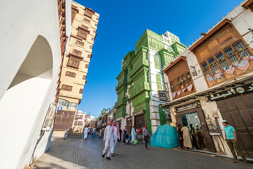 December 7th 2019, Jeddah, Saudi Arabia: The whole area (next to the green Noorwali House) was recently renovated and forms the main attraction of the old Jeddah nowadays. Many people (including two Saudi men in traditional clothes) are strolling along this street, as it leads into the Souk Baab Makkah, the traditional vegetable souk in Jeddah.