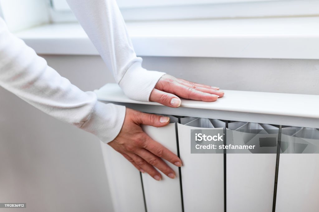 Heavy duty radiator - central heating. Woman is getting her hands warm on Home central heating system Radiator - Heater Stock Photo