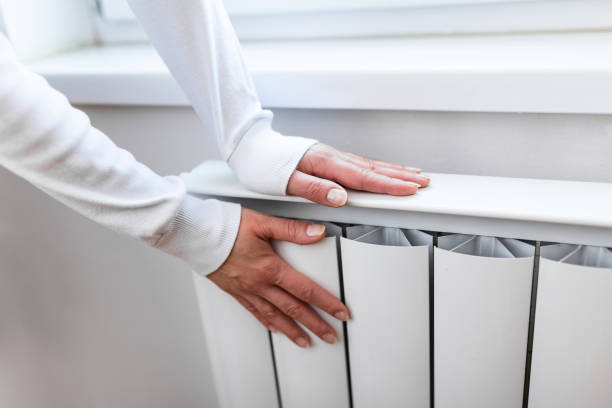 Heavy duty radiator - central heating. Woman is getting her hands warm on Home central heating system Heavy duty radiator - central heating. Woman is getting her hands warm on Home central heating system electric heater photos stock pictures, royalty-free photos & images