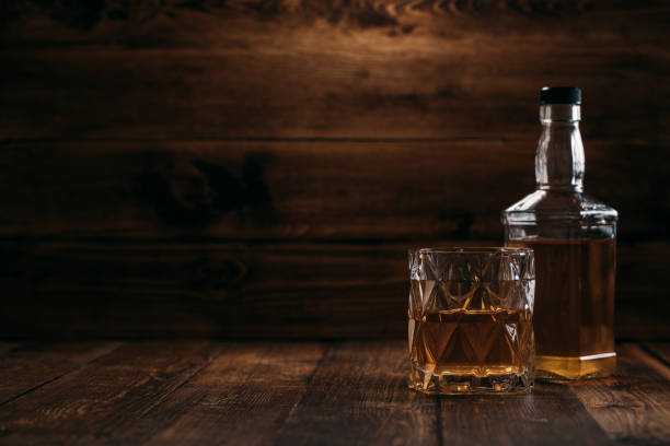 elegante bottiglia di whisky con bicchiere pieno su sfondo ligneo in stile retrò - cigar whisky bar cognac foto e immagini stock