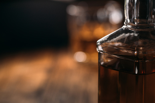 Macrophotos of a whiskey bottle in dim light on a wooden background.