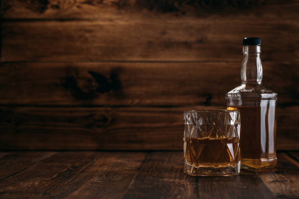 frasco elegante do uísque com um vidro cheio em um fundo de madeira no estilo retro - brandy bottle alcohol studio shot - fotografias e filmes do acervo