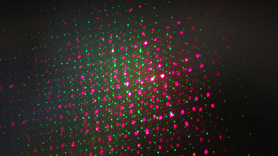 Many green and pink round dots misshapen shapes projected onto a black background with a beamer.