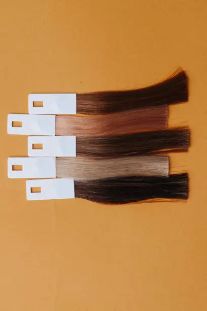 Photo of Smaples of dyed hair shot from above placed horizontally on orange surface.