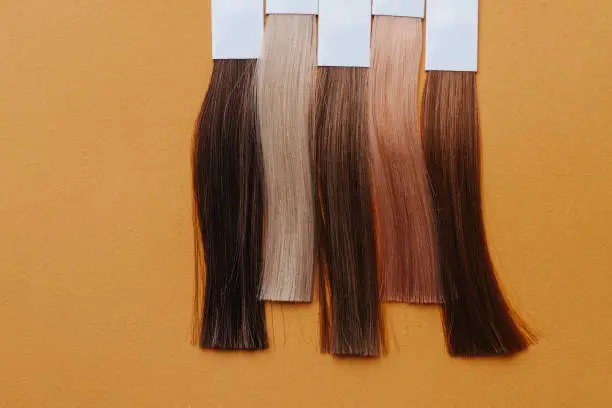 Photo of Vertical set of dyed hair locks. Samples in hairdressing salon on orange surface