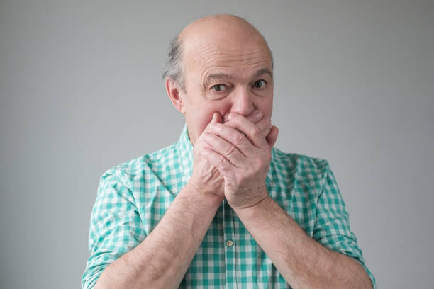 Mature senior hispanic men covering his mouth by hand stock photo