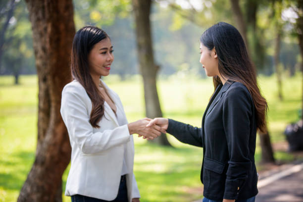 istock Side View Of Young Women Shaking Hands While Standing Against Trees 1192850087