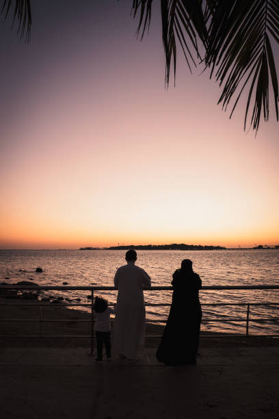 Arabic family standing at the South Corniche in Jeddah, Saudi Arabia, watching the beautiful and colorful sunset Family standing at the water's edge watching the sunset and waiting for the Jeddah Fountain to start ejecting the water. Jeddah, Saudi Arabia, December 8th 2019. saudi arabia jeddah landscape stock pictures, royalty-free photos & images