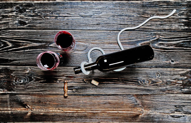 Direttamente sopra Shot Of Wine Bottle e bicchieri di vino con un vino rosso, cavatappi e un tappo di sughero girato su tavolo di legno rustico strutturato. - foto stock