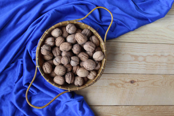 Top down view of a basket of walnuts in shells, on a wooden table with a background of classic blue table cloth. Natural food. With copyspace to the right.