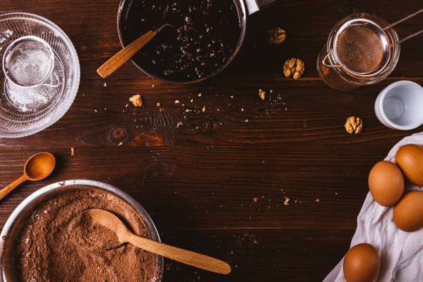 Chocolate bakery background Chocolate bakery background. Ingredients for making brownies, cocoa powder mixed with flour, walnuts, eggs and cooking utensils on dark wooden table, top view. walnut cookies stock pictures, royalty-free photos & images