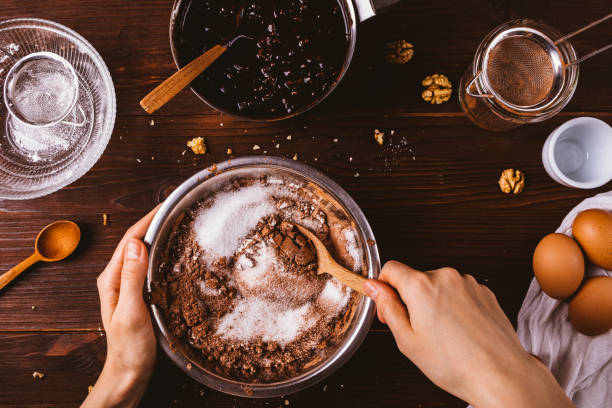 Top view female hands mix cocoa powder Top view female hands mix cocoa powder, sugar and flour to make dough with melted chocolate and walnuts for delicious homemade brownie cake. baked pastry item stock pictures, royalty-free photos & images