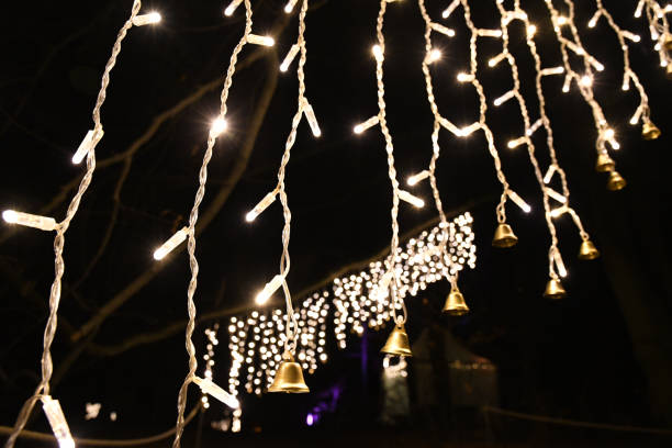 istock Night Christmas lighting decorations with shining string lights garlands and small shiny metal bells on dark background. Illuminated hanging lights. New Year celebration backdrop with copy space. 1192855020