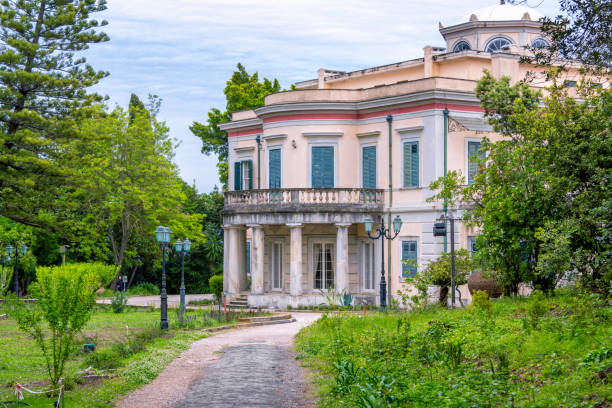 View of old villa Mon Repos on Corfu Island Corfu Island/Greece- May 4, 2019: view of old villa Mon Repos with columns, balcony and green wooden window shutters. Palace in a beautiful park. corfu holiday palace stock pictures, royalty-free photos & images