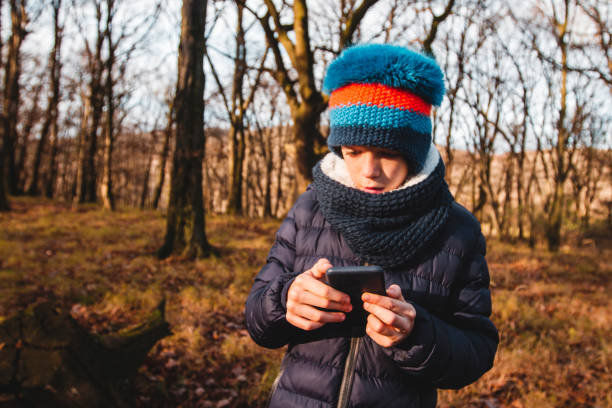 istock Boy with a funny blue and orange hat is using a smart phone in a forest 1192856404