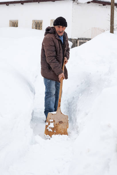 Mature adult man cleaning snow in front yard. He is using a wooden shovel. Shot in outdoor with a full frame DSLR camera.