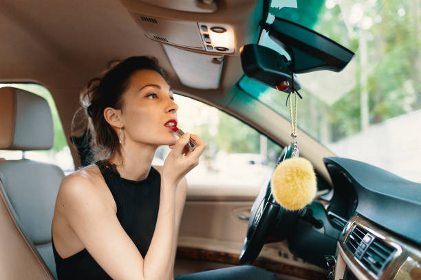 istock Young elegant woman looking in the car view mirror while applying makeup, lipstick on the lips 1192860229