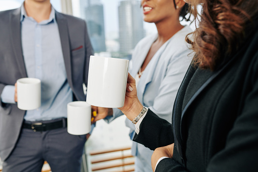 Businesswoman with big mug of coffee talking and gossiping with her coworkers during break