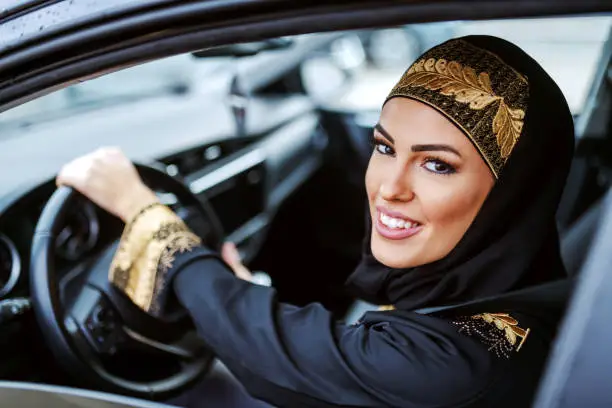 Photo of Young attractive smiling arab woman in traditional wear trying out new car.