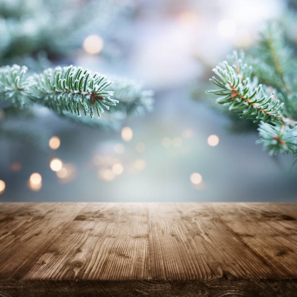 Fir branches in winter with table Frozen fir branches in winter with an empty wooden table in the foreground. Short depth of field and festive golden bokeh with space for christmas decorations. christmas market photos stock pictures, royalty-free photos & images