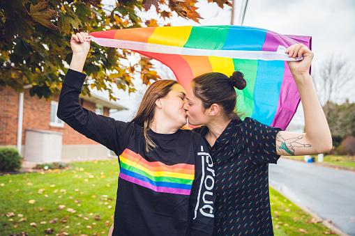 Lesbian, Love, Equality - Young Lesbian Couple kissing while flying a rainbow flag