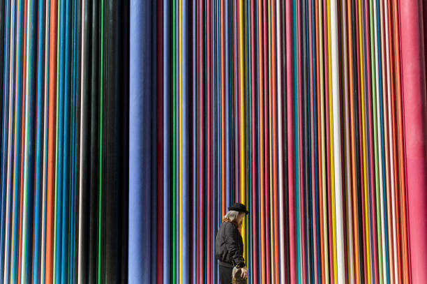 A woman wearing a hat walks past a wall made up of different color pipes running from top to bottom near the La Defense business area in Paris .