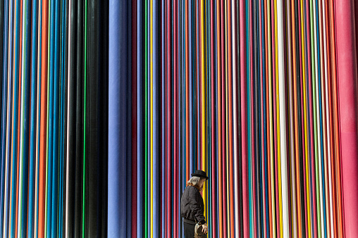 A woman wearing a hat walks past a wall made up of different color pipes running from top to bottom near the La Defense business area in Paris .