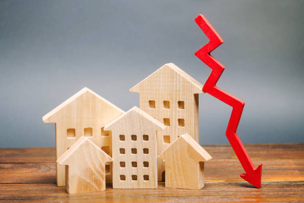 ミニチュア木造住宅と赤い矢印ダウン。低コストの不動産の概念。住宅ローン金利の引き下げ。賃貸住宅やマンションの価格下落。住宅購入需要の削減 - 低下させる ストックフォトと画像
