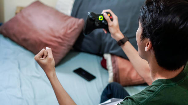 millennials asiatici emotivi che giocano a videogiochi a letto - overemotional foto e immagini stock