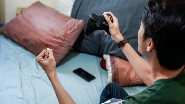 overemotional asian millennials playing video game in bed - overemotional imagens e fotografias de stock