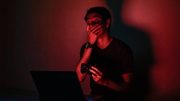 чрезмерно эмоциональный азиатских millennials играть видео игры в темной комнате красный фон - overemotional стоковые фото и изображения