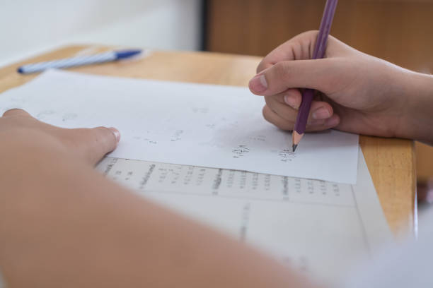 istock Students hands taking exams, writing examination room with holding pencil on optical form of standardized test with answers and english paper sheet on row desk chair doing final exam in classroom. 1192870432