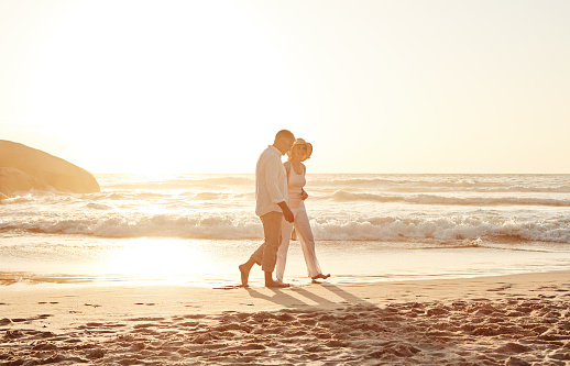 Full length shot of an affectionate middle aged couple walking hand in hand along the beach at sunset
