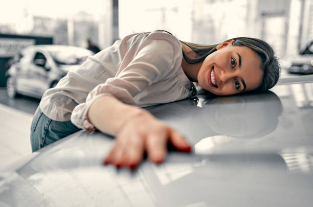 Visit to the dealership. Beautiful woman hugging and showing her love to a car in a car showroom. car ownership photos stock pictures, royalty-free photos & images