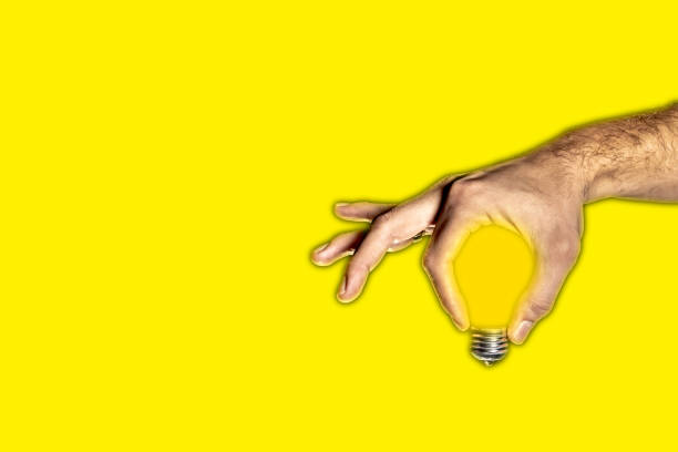 istock Light bulb in human hand - yellow background 1192871988