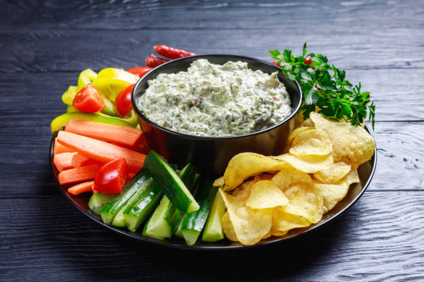 Creamy spinach dip in a bowl with sausages, carrots, cucumber, sweet pepper sticks, potato chips and fresh parsley on a plate close-up of Creamy spinach dip in a bowl with sausages, carrots, cucumber, sweet pepper sticks, potato chips and fresh parsley on a plate dipping stock pictures, royalty-free photos & images