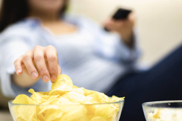 Unrecognizable woman is eating potato chips. Close up huge deep plate, full of potato chips. Concept take potato chips with you to watch movie. Close up. Blurred background. crisps stock pictures, royalty-free photos & images