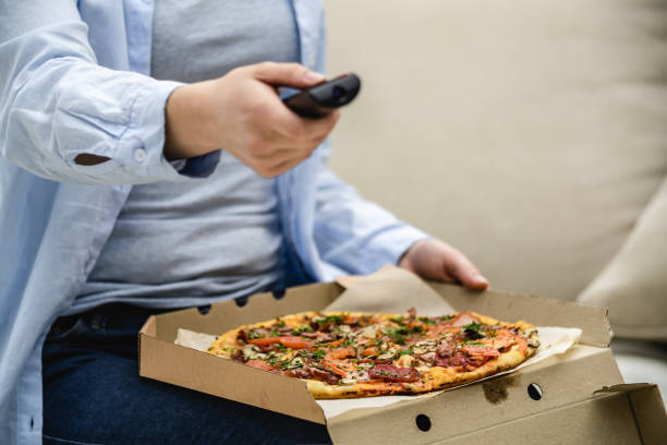 istock Crop. Unrecognizable woman is sitting on her sofa at home and is watching television while eating pizza. Copy space. 1192879142