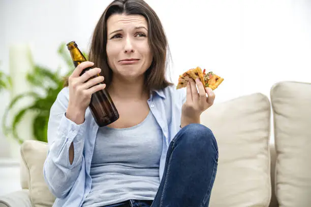 Photo of Brunette woman is scared, because of TV programmes. She is stressed. Woman is trying to heal her pain with a help of snacks. Close up.