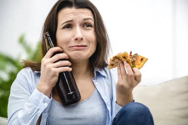 Photo of Brunette woman is scared, because of TV programmes. She is stressed. Woman is trying to heal her pain with a help of snacks. Close up.