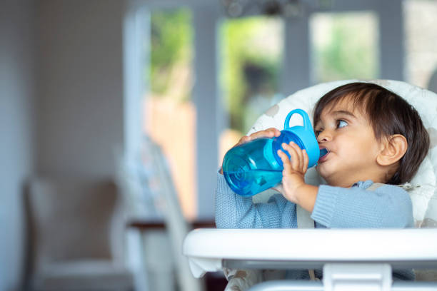 Drinking Water in High Chair A front-view shot of a young boy drinking water from a reusable water bottle at home, he is wearing casual clothing and sitting in a high chair. blue reusable water bottle stock pictures, royalty-free photos & images