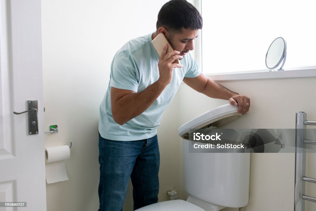 Broken Toilet A side-view shot of a man standing in his bathroom looking at his toilet, there is a problem, he is on the phone trying to call a plumber. Toilet Stock Photo