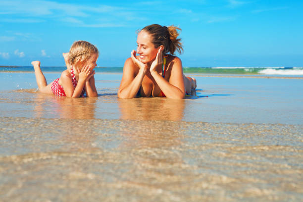Mother with child lying in water pool at sea beach Happy people have fun in sea surf on white sand beach. Young mother with child lying in water pool. Travel lifestyle, swimming activities in family summer camp. Vacations with kids on tropical island. phuket beach party stock pictures, royalty-free photos & images