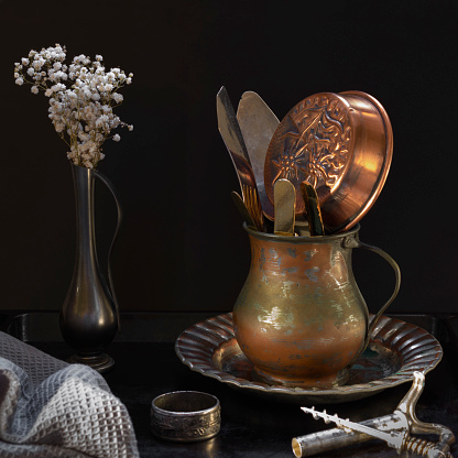Vintage kitchen utensils: corkscrew, vase of flowers, napkin ring, plate, knife, fork, pan on black background. Still life, front view