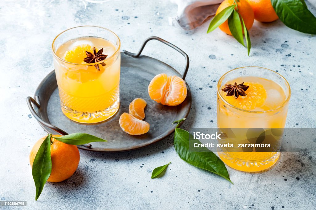Spicy winter yellow orange cocktail or mocktail with fresh tangerines and anise on grey background. Christmas and New Year holiday welcome drink, copy space Mocktail Stock Photo