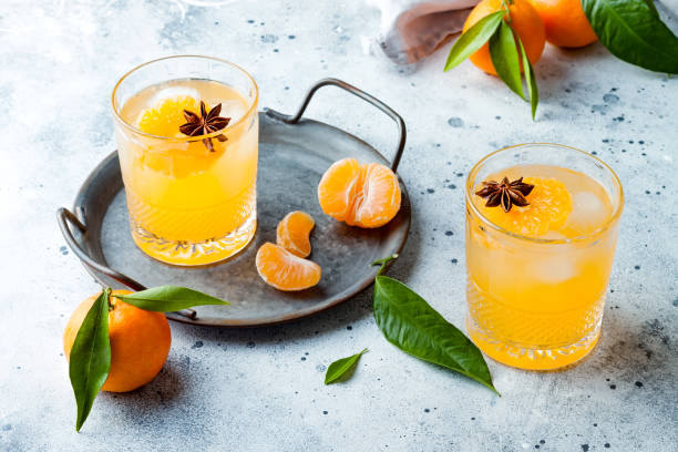 Spicy winter yellow orange cocktail or mocktail with fresh tangerines and anise on grey background. Christmas and New Year holiday welcome drink, copy space stock photo
