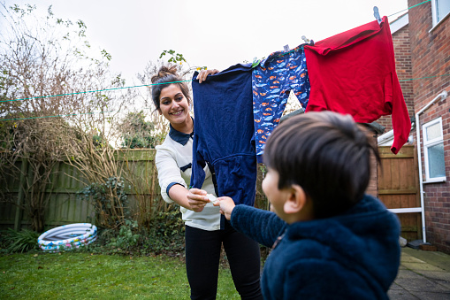 A close-up shot of a cheerful woman hanging laundry on the washing line in the garden, her young son is helping her.